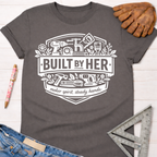 Charcoal gray "Built By Her" graphic tee with tools, "maker spirit, steady hands" text, and rolled sleeves. Women's funny woodworking graphic tee shirt for female woodworkers, makers, and DIY builders — Sawdust & Ponytails