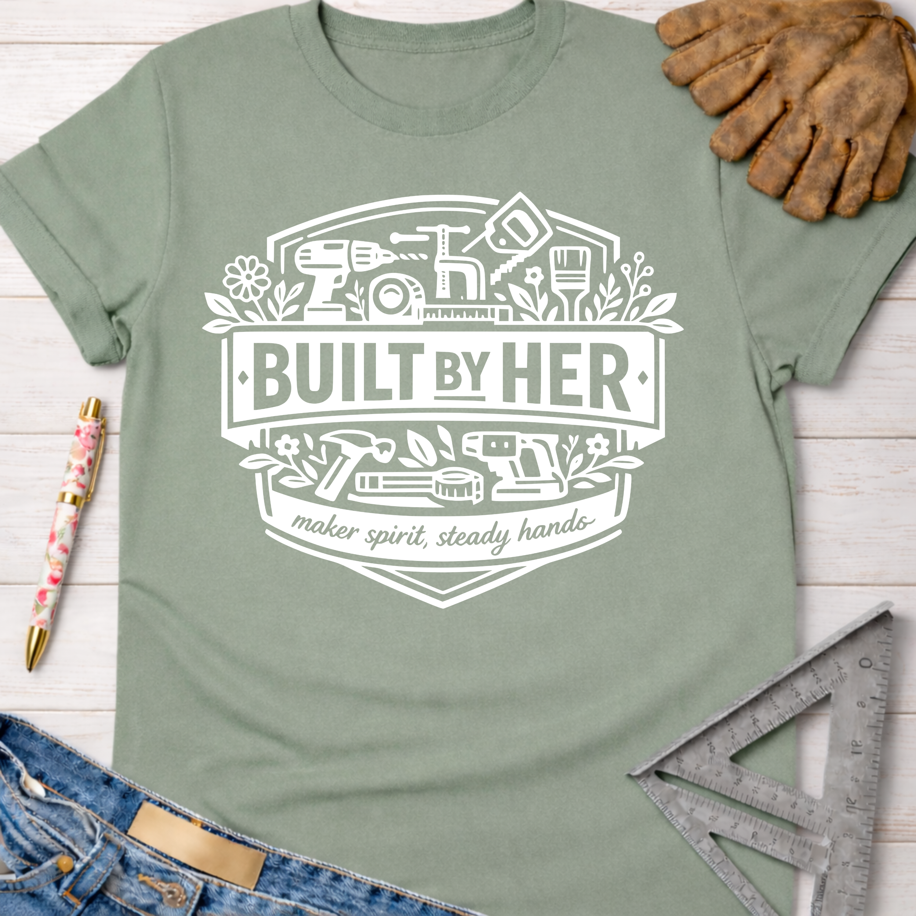 Women's funny woodworking graphic tee shirt for female woodworkers, makers, and DIY builders — Sawdust & Ponytails. Sage green t-shirt with "Built By Her" tools graphic.