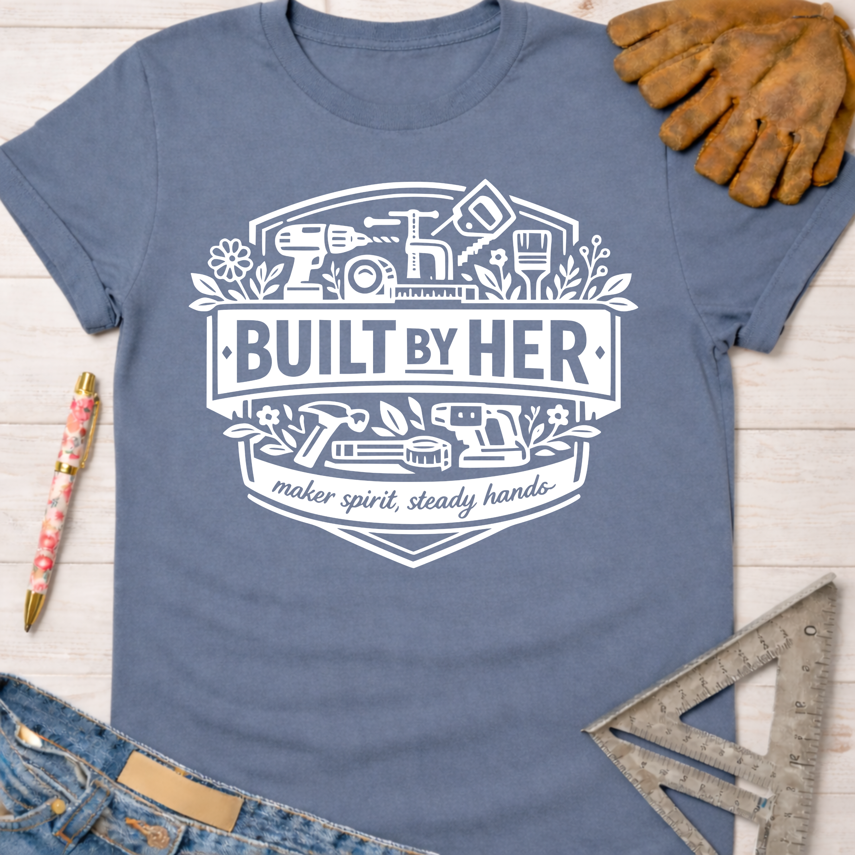 Women's funny woodworking graphic tee shirt for female woodworkers, makers, and DIY builders — Sawdust & Ponytails. Blue cotton tee with "Built By Her" and tool graphic.