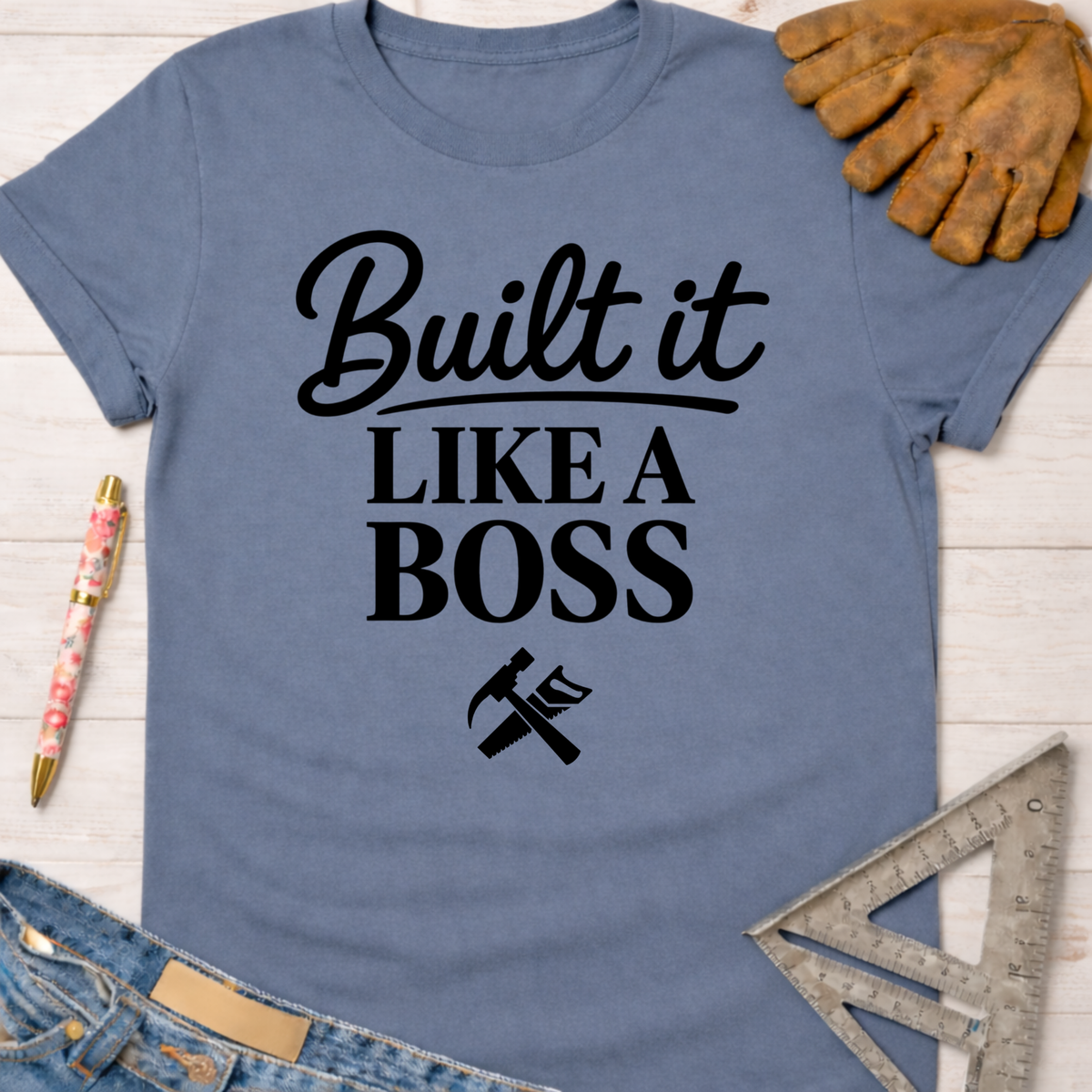 Women's funny woodworking graphic tee shirt for female woodworkers, makers, and DIY builders — Sawdust & Ponytails. Blue cotton t-shirt with "Built It Like a Boss" text and hammer/saw graphic.
