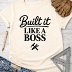 Women's funny woodworking graphic tee shirt for female woodworkers, makers, and DIY builders — Sawdust & Ponytails. Cream t-shirt with "Built It LIKE A BOSS" in black text, hammer and saw graphic.