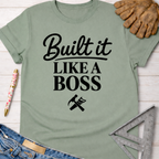 Women's funny woodworking graphic tee shirt for female woodworkers, makers, and DIY builders — Sawdust & Ponytails. Sage green cotton tee with "Built It Like a Boss" text and tools.