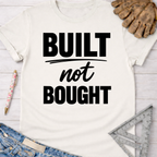 Women's funny woodworking graphic tee shirt for female woodworkers, makers, and DIY builders — Sawdust & Ponytails. Cream t-shirt with "Built not Bought" in black text.