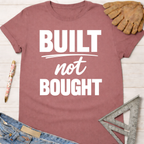 Women's funny woodworking graphic tee shirt for female woodworkers, makers, and DIY builders — Sawdust & Ponytails. Mauve "Built Not Bought" t-shirt with jeans, work glove, and ruler.