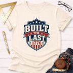 Cream "Built To Last 1776" badge t-shirt with red, white, and blue design, styled with jeans.