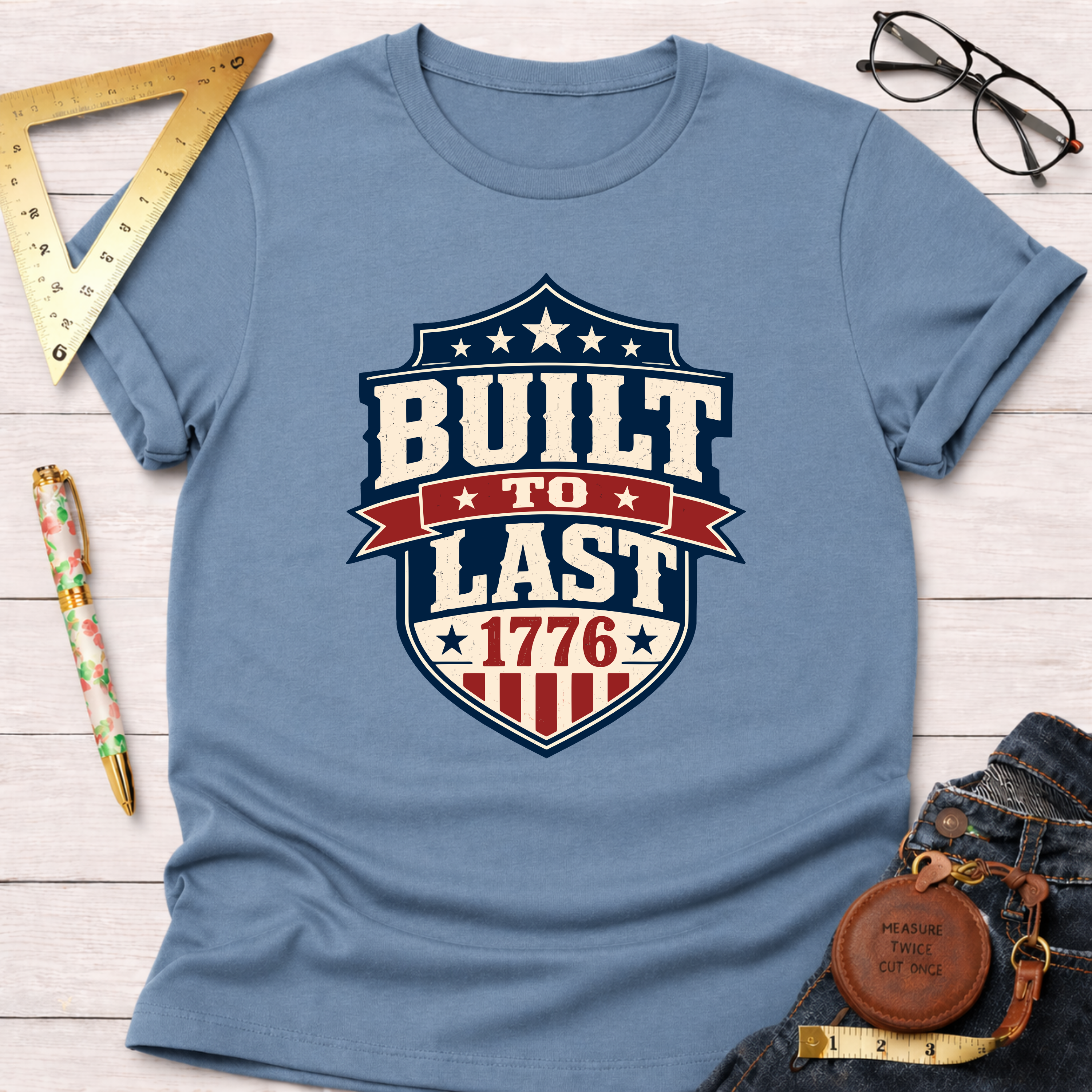 Light blue cotton t-shirt with a red, white, and blue "Built To Last 1776" badge design.