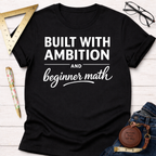 Black cotton tee with "Built With Ambition And Beginner Math" in white text. Women's funny woodworking graphic tee shirt for female woodworkers, makers, and DIY builders — Sawdust & Ponytails.