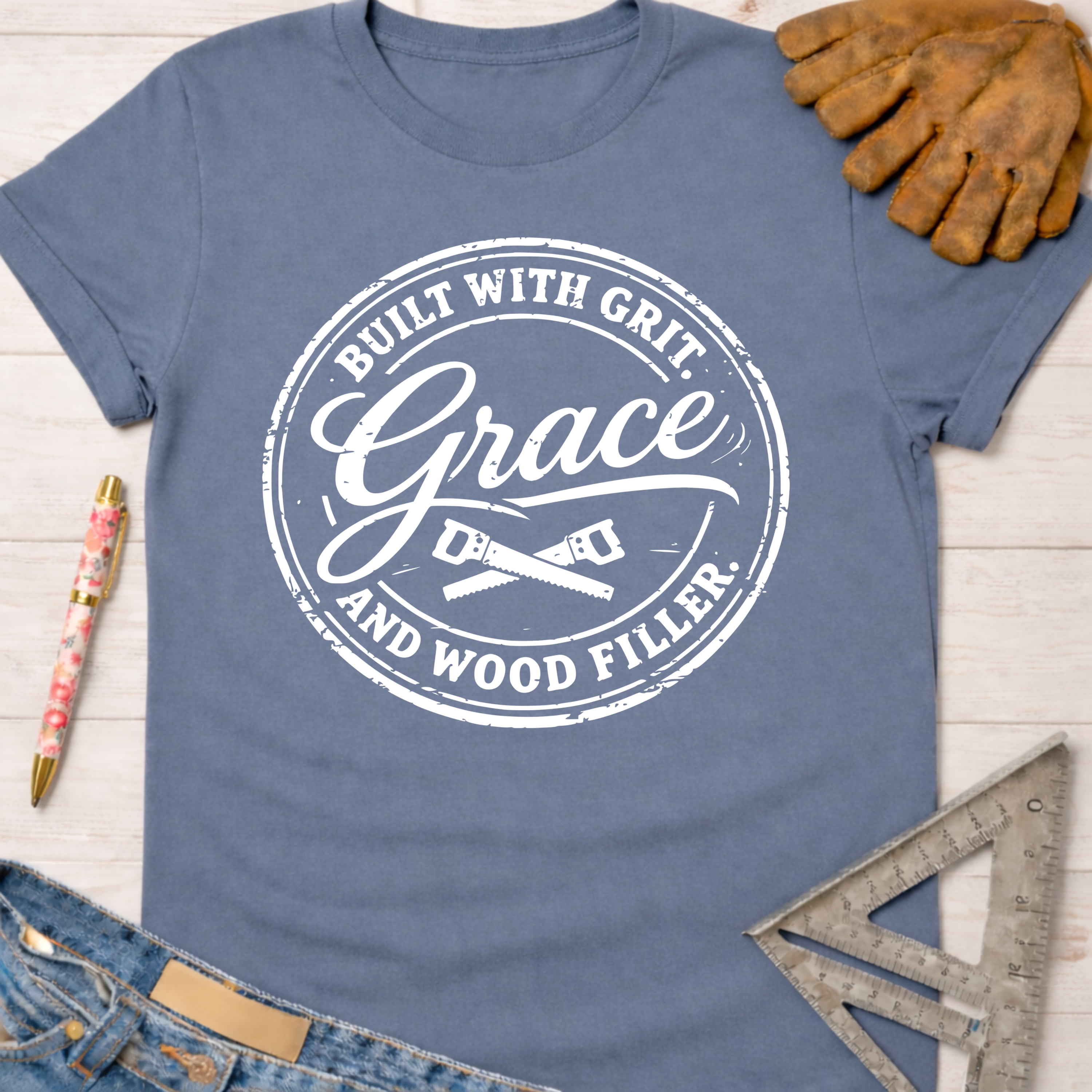 Women's funny woodworking graphic tee shirt for female woodworkers, makers, and DIY builders — Sawdust & Ponytails. Blue cotton tee with "Built With Grit, Grace, and Wood Filler" graphic.