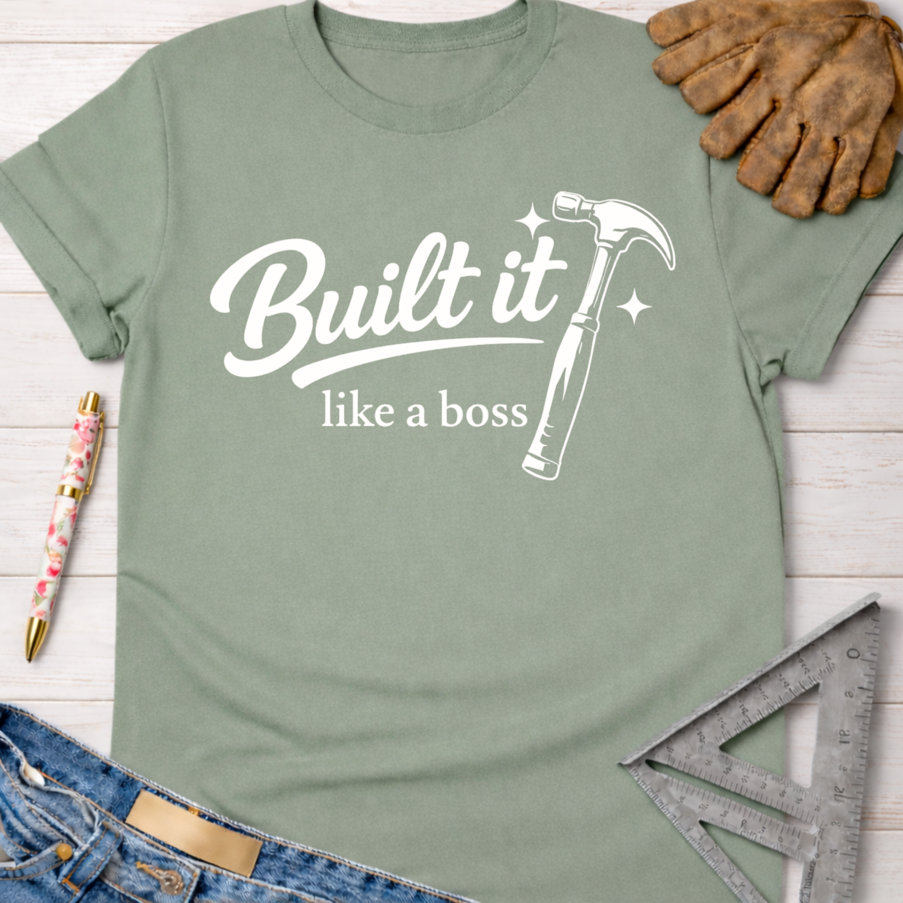 Women's funny woodworking graphic tee shirt for female woodworkers, makers, and DIY builders — Sawdust & Ponytails. Sage green cotton t-shirt with "Built it like a boss" text and a hammer graphic.