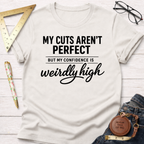 Women's funny woodworking graphic tee shirt for female woodworkers, makers, and DIY builders — Sawdust & Ponytails. Cream t-shirt with "My Cuts Aren't Perfect But My Confidence Is Weirdly High" text.