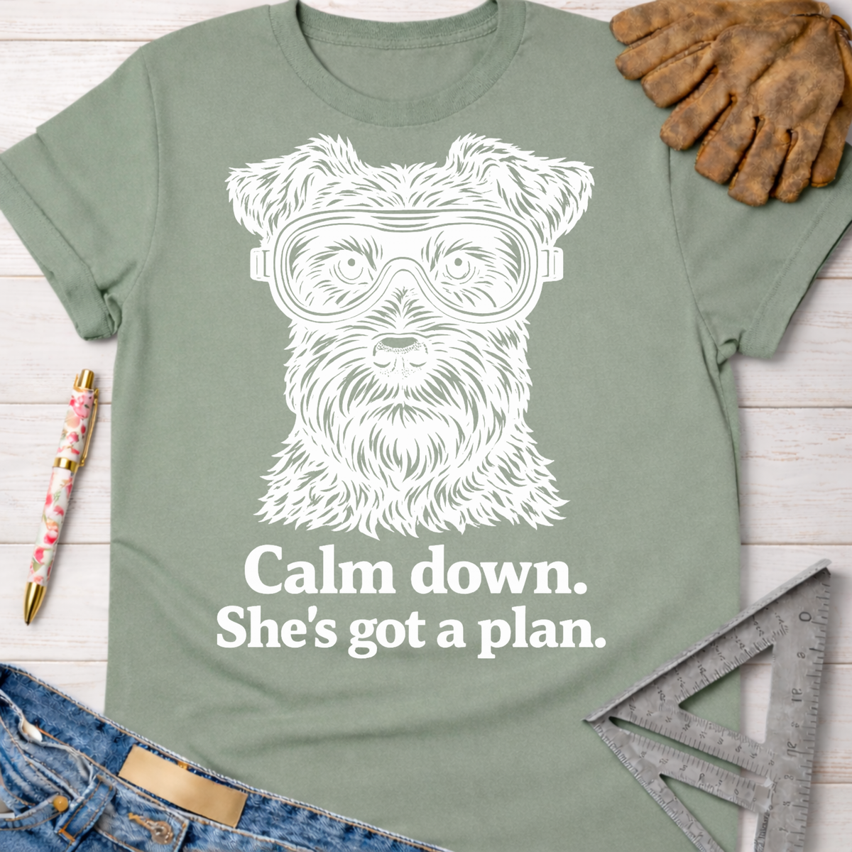 Women's funny woodworking graphic tee shirt for female woodworkers, makers, and DIY builders — Sawdust & Ponytails. Sage green cotton t-shirt with a white graphic of a dog wearing safety goggles and "Calm down. She's got a plan." text.