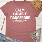 Women's funny woodworking graphic tee shirt for female woodworkers, makers, and DIY builders — Sawdust & Ponytails. Dusty rose t-shirt with "Calm. Capable. Dangerous with power tools" in white text.