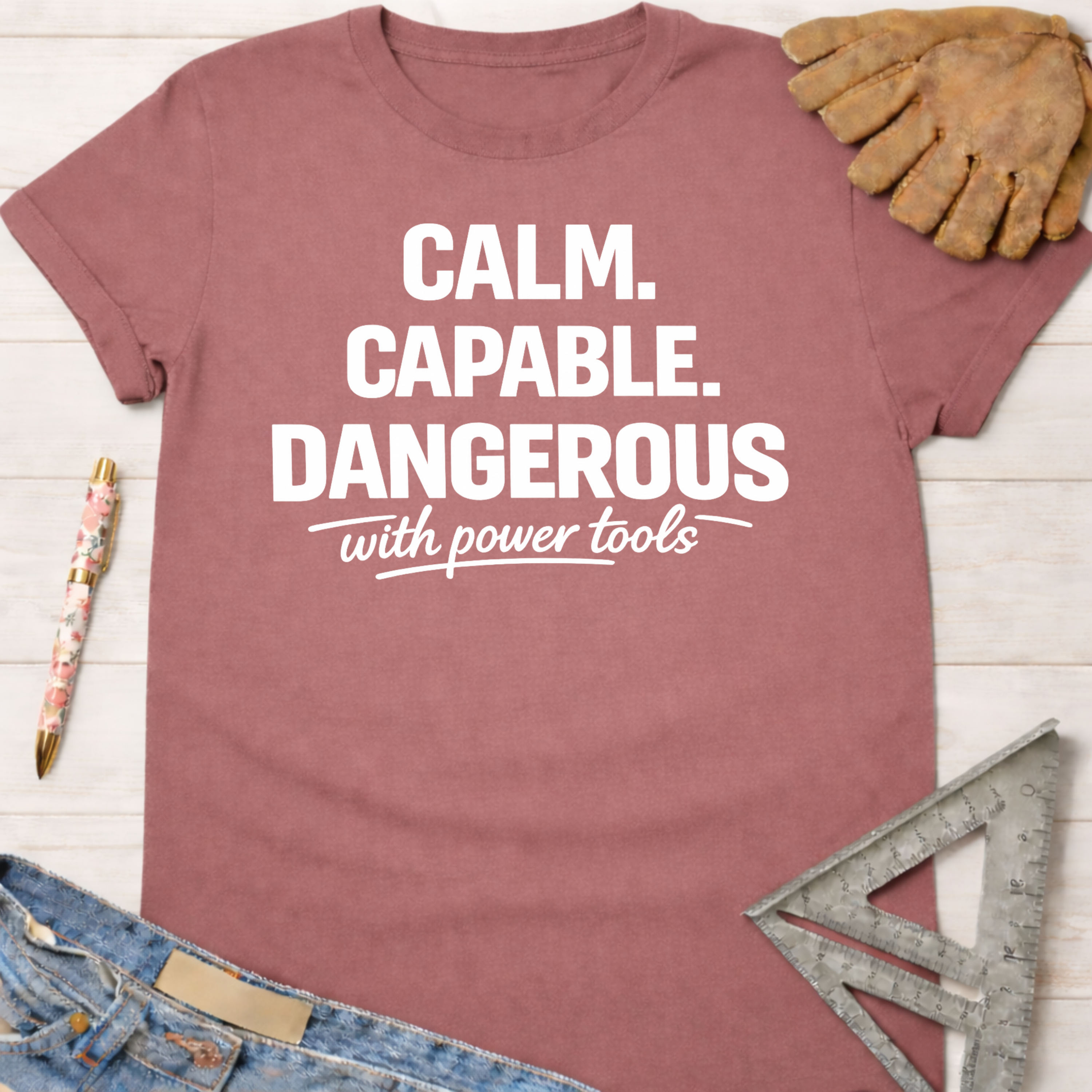 Women's funny woodworking graphic tee shirt for female woodworkers, makers, and DIY builders — Sawdust & Ponytails. Dusty rose t-shirt with "Calm. Capable. Dangerous with power tools" in white text.