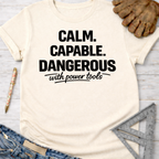 Women's funny woodworking graphic tee shirt for female woodworkers, makers, and DIY builders — Sawdust & Ponytails. Cream t-shirt with "Calm. Capable. Dangerous with power tools" in black text.