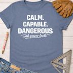Women's funny woodworking graphic tee shirt for female woodworkers, makers, and DIY builders — Sawdust & Ponytails. Blue cotton t-shirt with "Calm. Capable. Dangerous with power tools" in white text.
