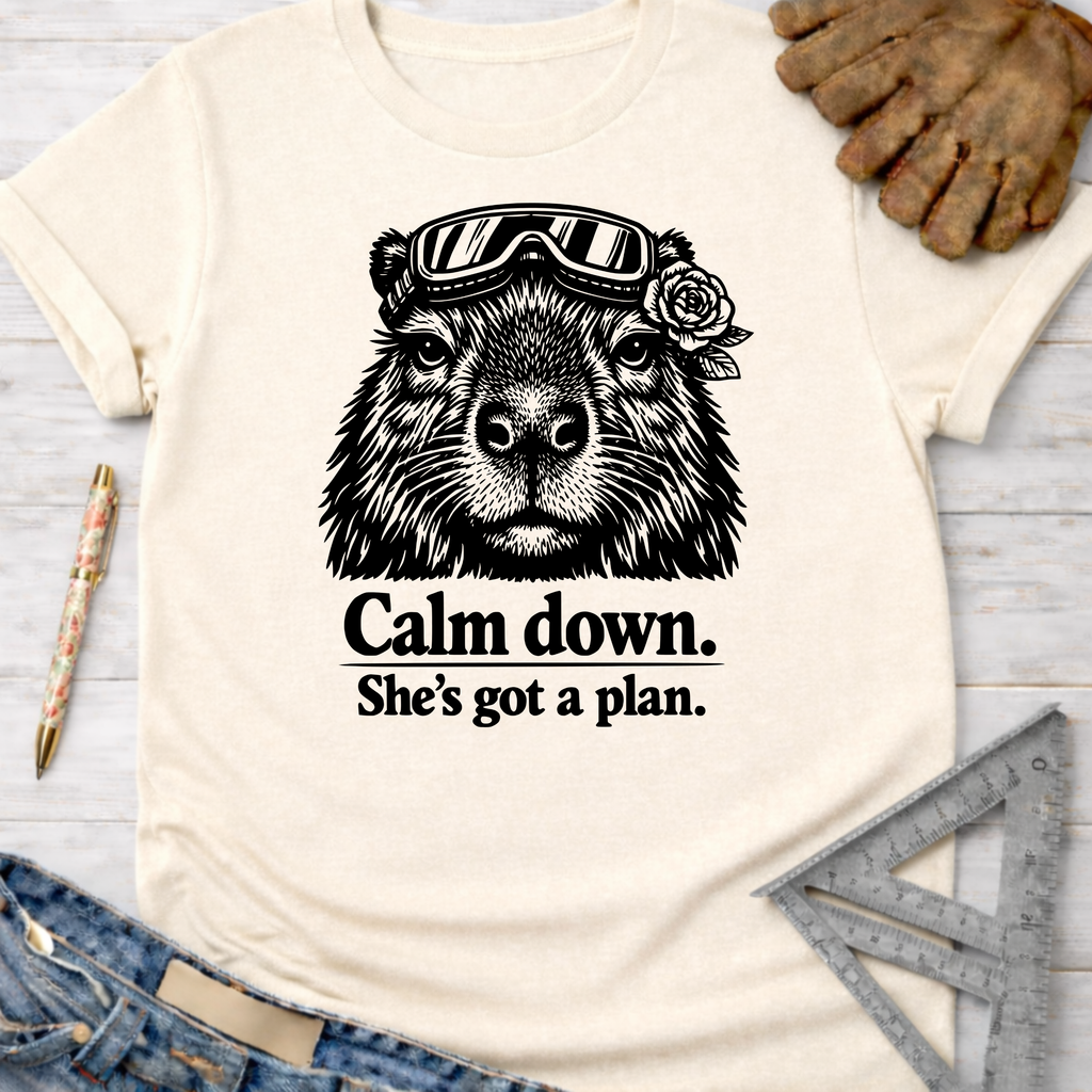 Women's funny woodworking graphic tee shirt for female woodworkers, makers, and DIY builders — Sawdust & Ponytails. Cream crewneck t-shirt with a black graphic of a capybara wearing goggles and a rose, with the text "Calm down. She's got a plan.