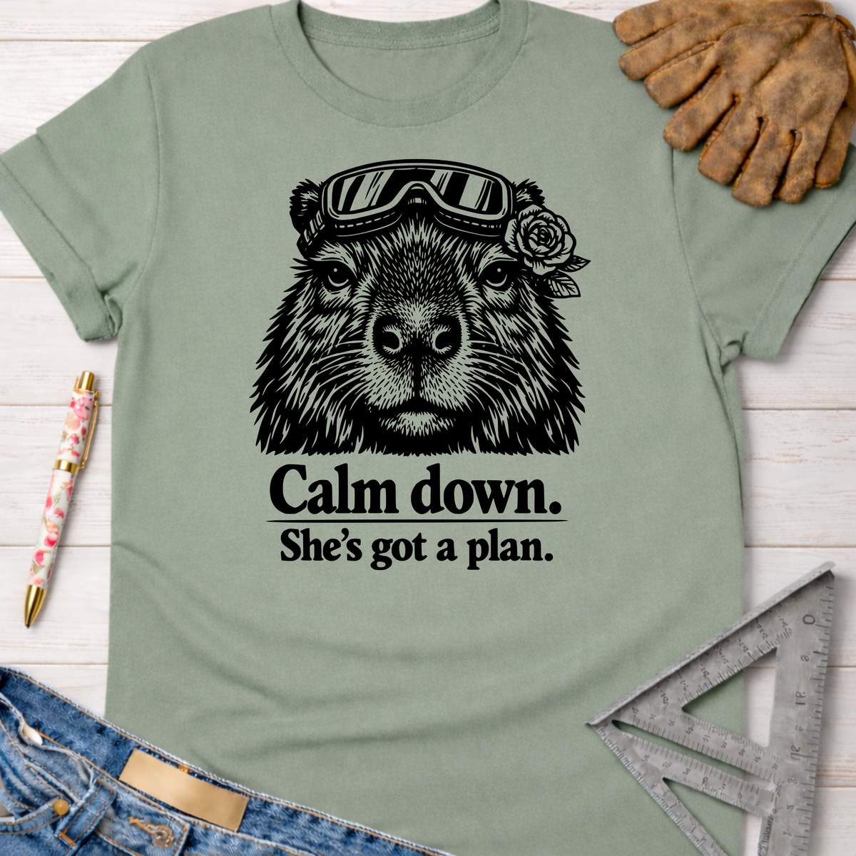Women's funny woodworking graphic tee shirt for female woodworkers, makers, and DIY builders — Sawdust & Ponytails. Sage green cotton tee with a black graphic of a capybara wearing goggles and a rose, text reads "Calm down. She's got a plan.