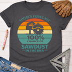 Women's funny woodworking graphic tee shirt for female woodworkers, makers, and DIY builders — Sawdust & Ponytails. Dark gray t-shirt with a retro sunset graphic featuring a circular saw and the text "Today's Forecast 100% Chance of Sawdust in the Bra.