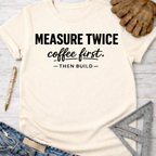 Women's funny woodworking graphic tee shirt for female woodworkers, makers, and DIY builders — Sawdust & Ponytails. Cream t-shirt with "MEASURE TWICE coffee first. — THEN BUILD —" in black text.