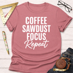 Pink short-sleeve t-shirt with "Coffee Sawdust Focus Repeat" in white text, styled with jeans and tools.