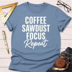 Light blue cotton t-shirt with "Coffee Sawdust Focus Repeat" in white text, styled with jeans and tools.