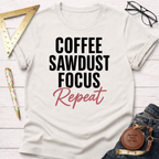 Cream cotton t-shirt with "Coffee Sawdust Focus Repeat" in black and pink text, styled with jeans and tools.
