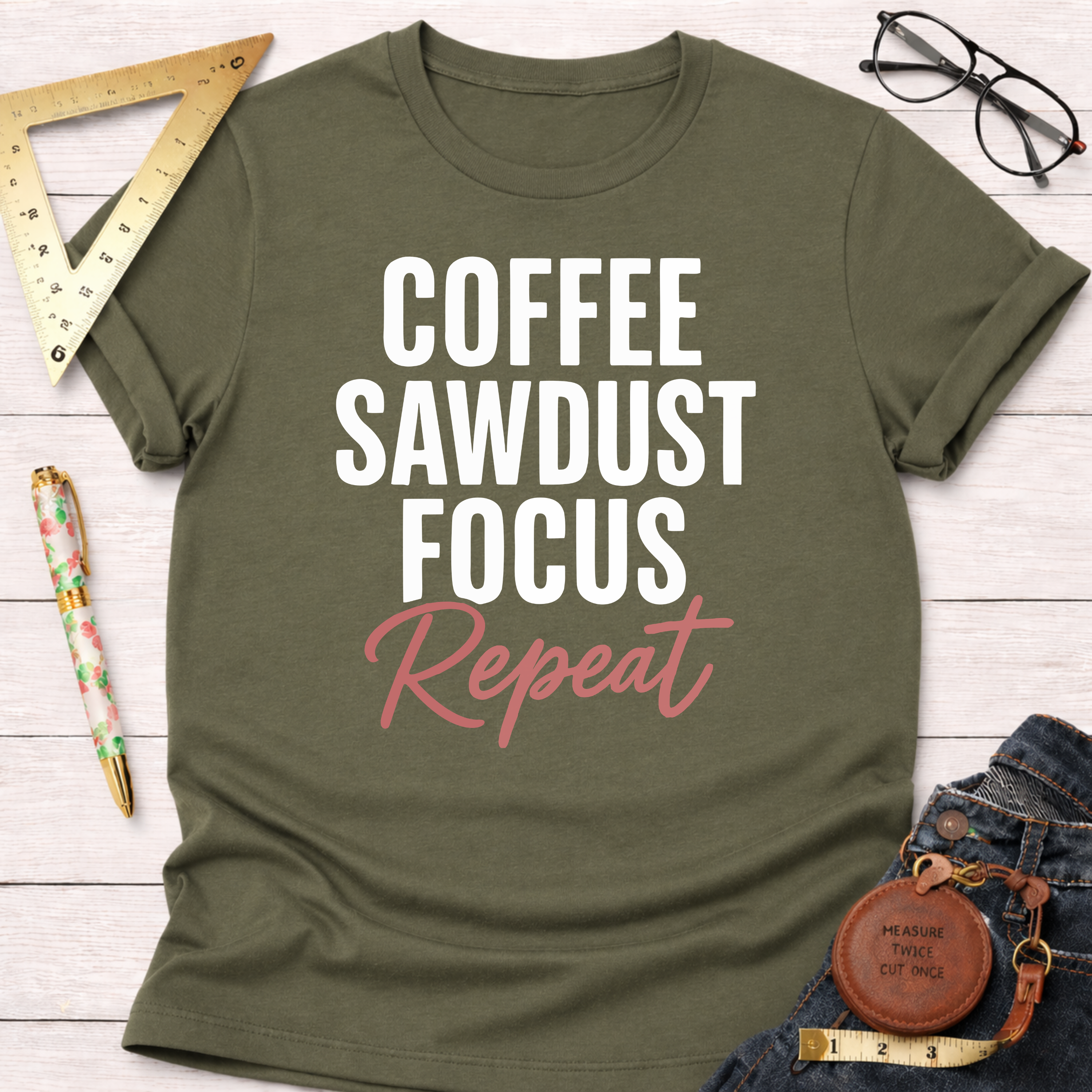 Olive green t-shirt with "COFFEE SAWDUST FOCUS" in white and "Repeat" in pink, styled with jeans and tools.