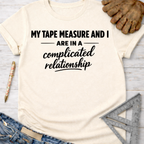 Women's funny woodworking graphic tee shirt for female woodworkers, makers, and DIY builders — Sawdust & Ponytails. Cream short-sleeve tee with "My Tape Measure And I Are In A Complicated Relationship" text.