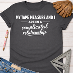 Charcoal gray "Complicated Relationship" tee with white text, denim, work glove, and ruler. Women's funny woodworking graphic tee shirt for female woodworkers, makers, and DIY builders — Sawdust & Ponytails