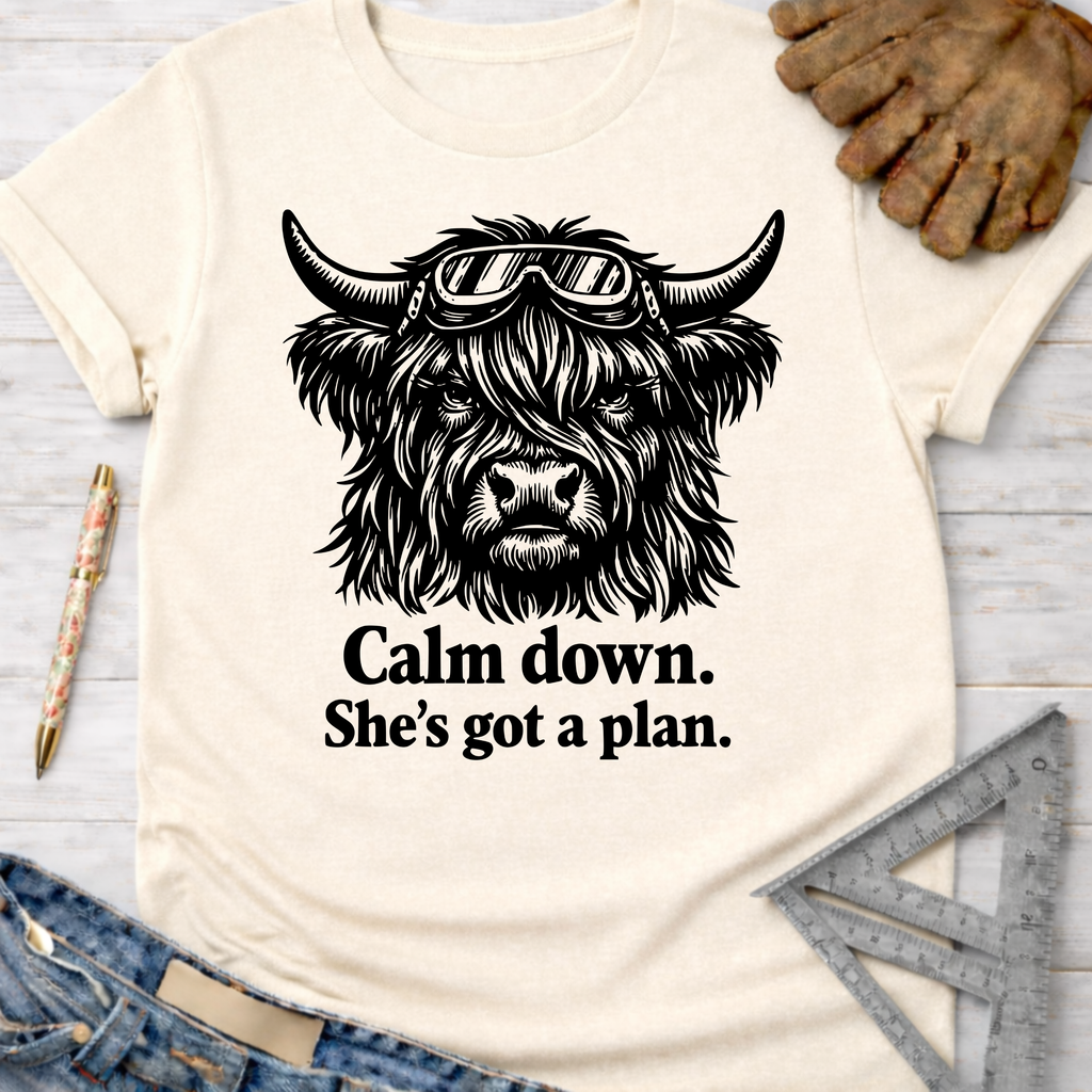 Women's funny woodworking graphic tee shirt for female woodworkers, makers, and DIY builders — Sawdust & Ponytails. Cream short-sleeve t-shirt with a black graphic of a Highland cow wearing goggles and text "Calm down. She's got a plan.