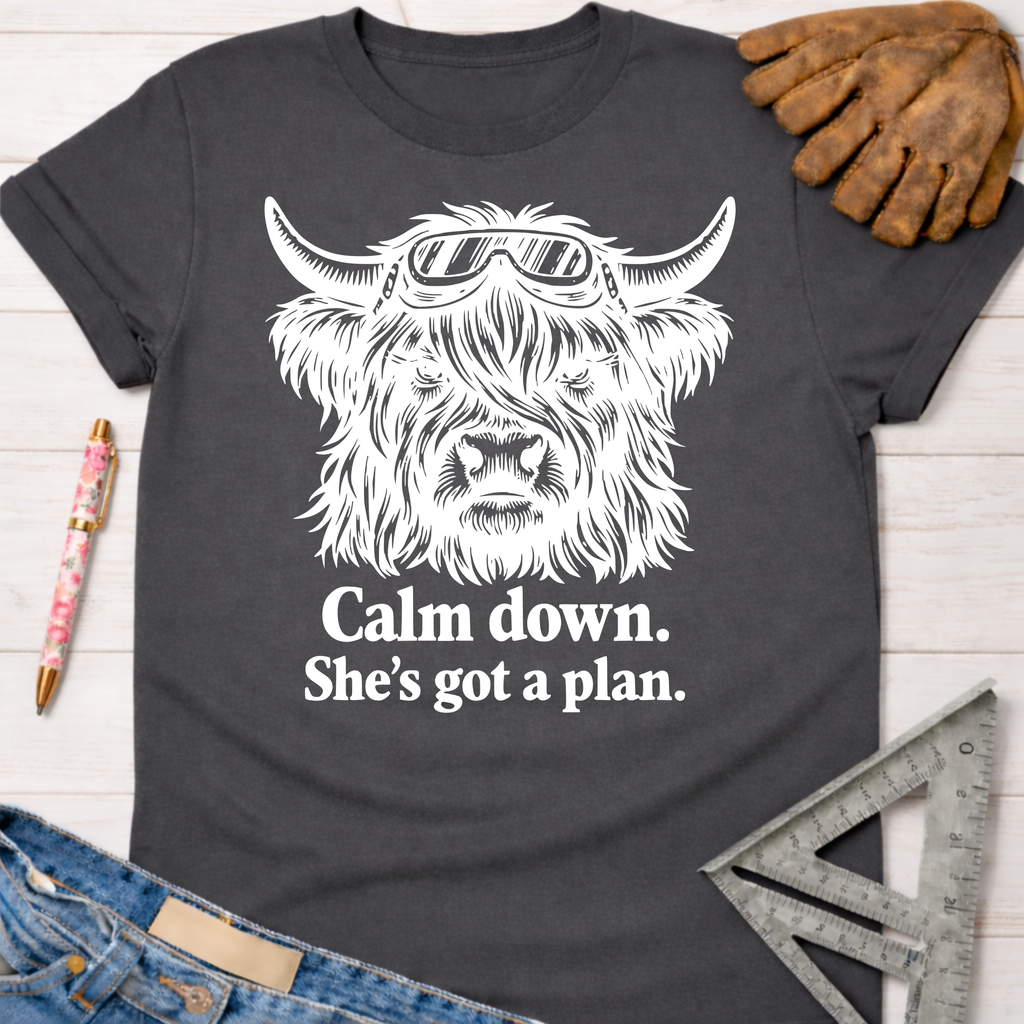 Women's funny woodworking graphic tee shirt for female woodworkers, makers, and DIY builders — Sawdust & Ponytails. Dark gray t-shirt with a white graphic of a Highland cow wearing goggles and text "Calm down. She's got a plan.