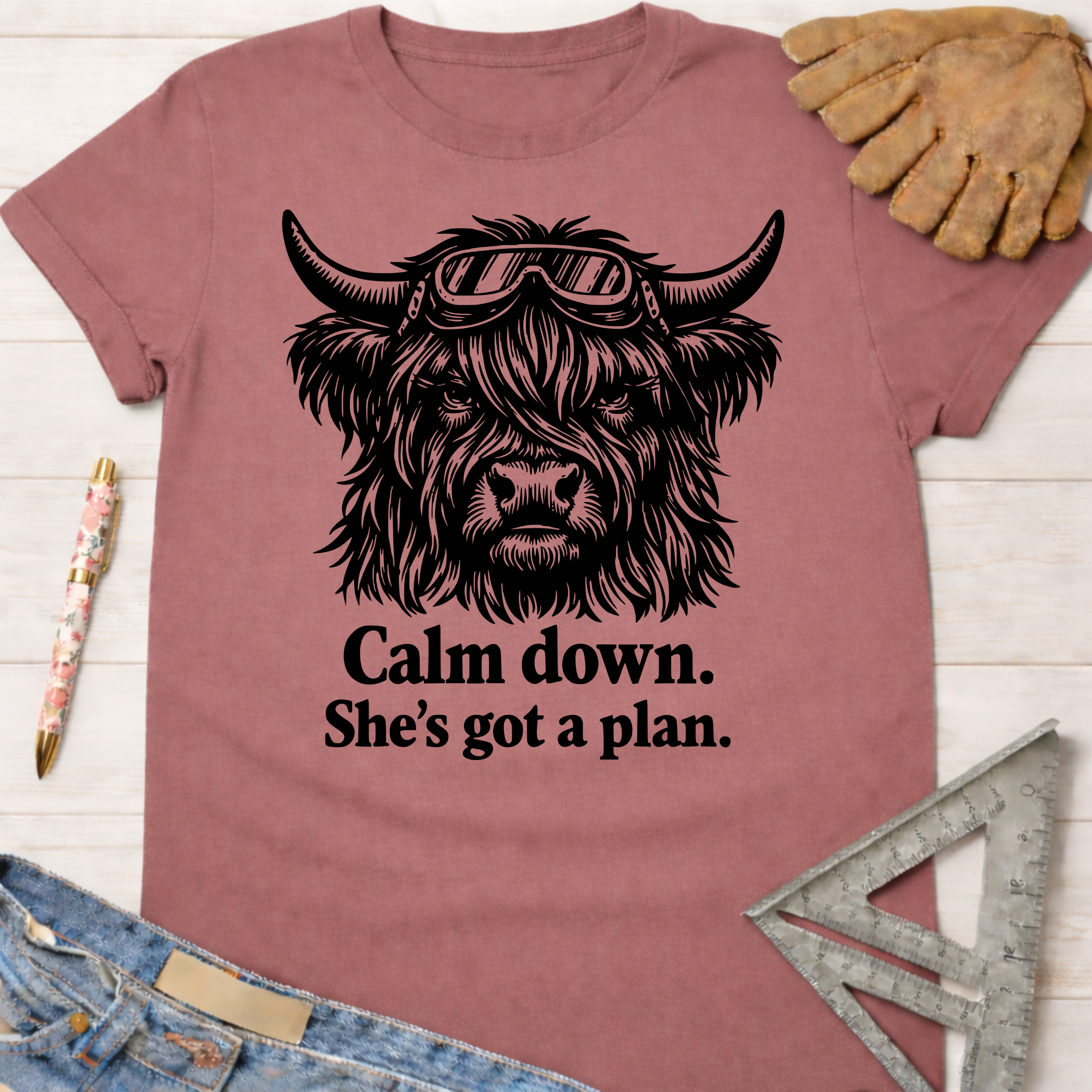 Women's funny woodworking graphic tee shirt for female woodworkers, makers, and DIY builders — Sawdust & Ponytails. Mauve t-shirt with a black graphic of a highland cow wearing goggles and the text "Calm down. She's got a plan.