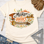 Women's funny woodworking graphic tee shirt for female woodworkers, makers, and DIY builders — Sawdust & Ponytails. Cream t-shirt with "Maker at Heart: Crafting My Own Path" graphic, featuring tools, mountains, and a birdhouse.