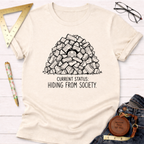 Cream t-shirt with "Current Status: Hiding From Society" text and a person peeking from a woodpile.