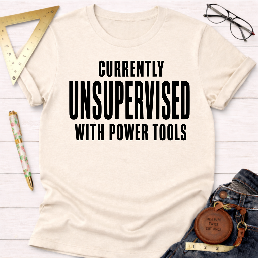 Women's funny woodworking graphic tee shirt for female woodworkers, makers, and DIY builders — Sawdust & Ponytails. Cream cotton t-shirt with "CURRENTLY UNSUPERVISED WITH POWER TOOLS" in black text.