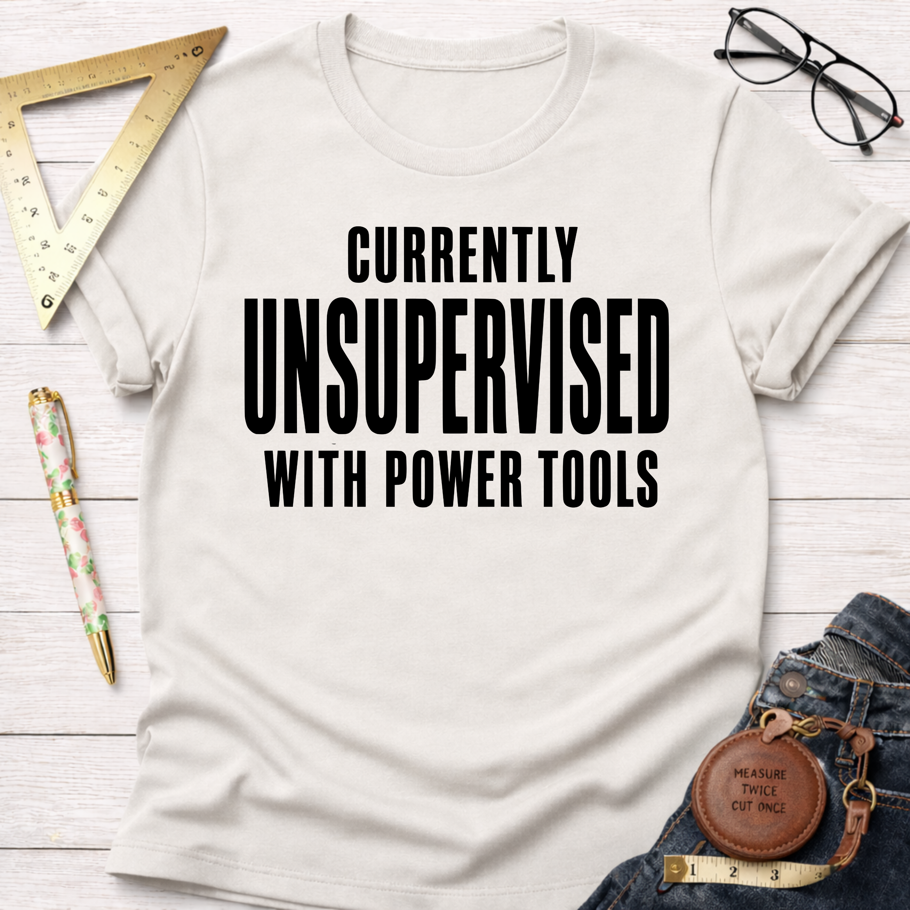Women's funny woodworking graphic tee shirt for female woodworkers, makers, and DIY builders — Sawdust & Ponytails. Cream t-shirt with "CURRENTLY UNSUPERVISED WITH POWER TOOLS" in black text.