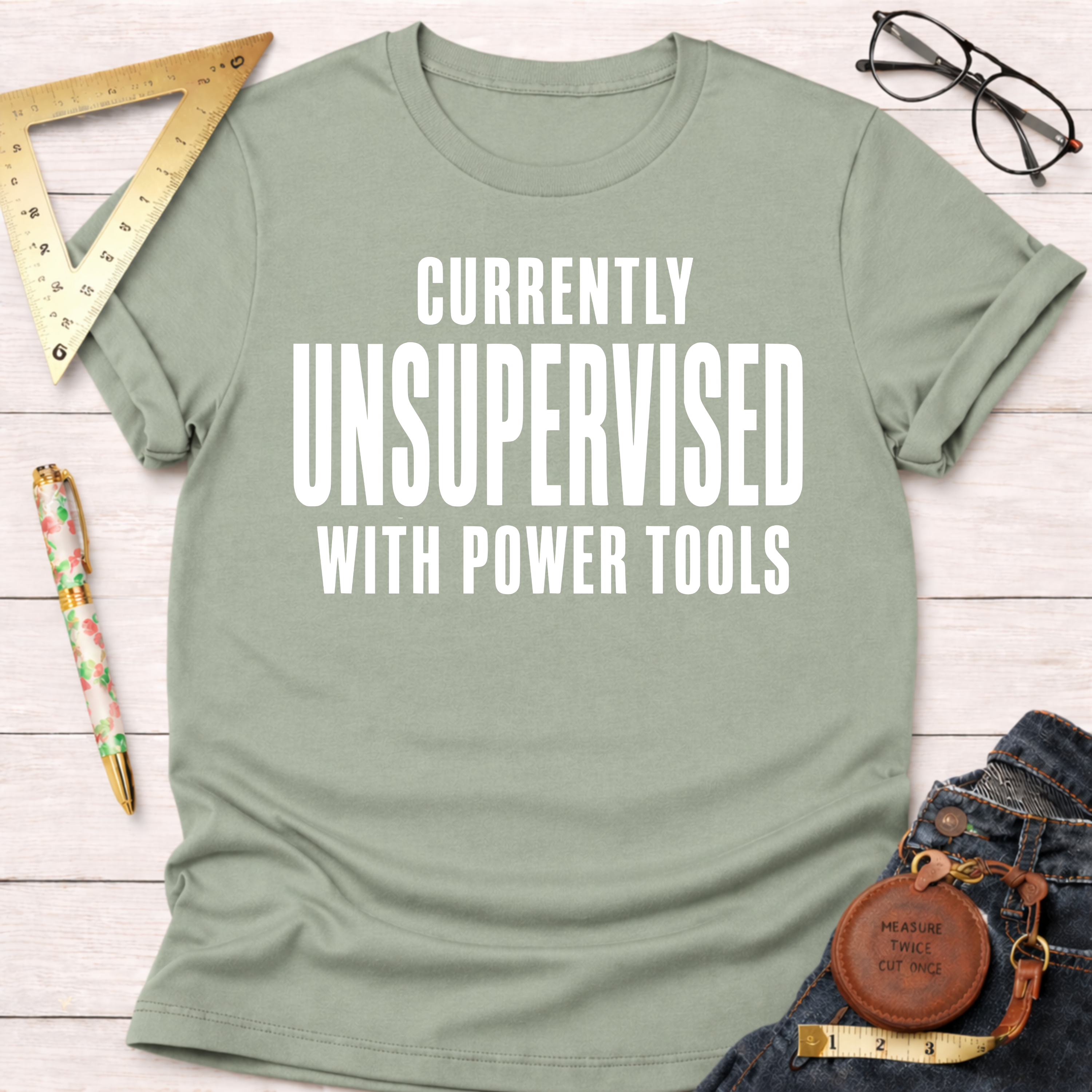 Women's funny woodworking graphic tee shirt for female woodworkers, makers, and DIY builders — Sawdust & Ponytails. Light green cotton tee with "CURRENTLY UNSUPERVISED WITH POWER TOOLS" in white text.