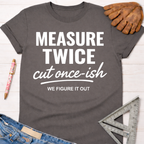 Women's funny woodworking graphic tee shirt for female woodworkers, makers, and DIY builders — Sawdust & Ponytails. Dark gray cotton tee with "MEASURE TWICE cut once-ish WE FIGURE IT OUT" in white text.