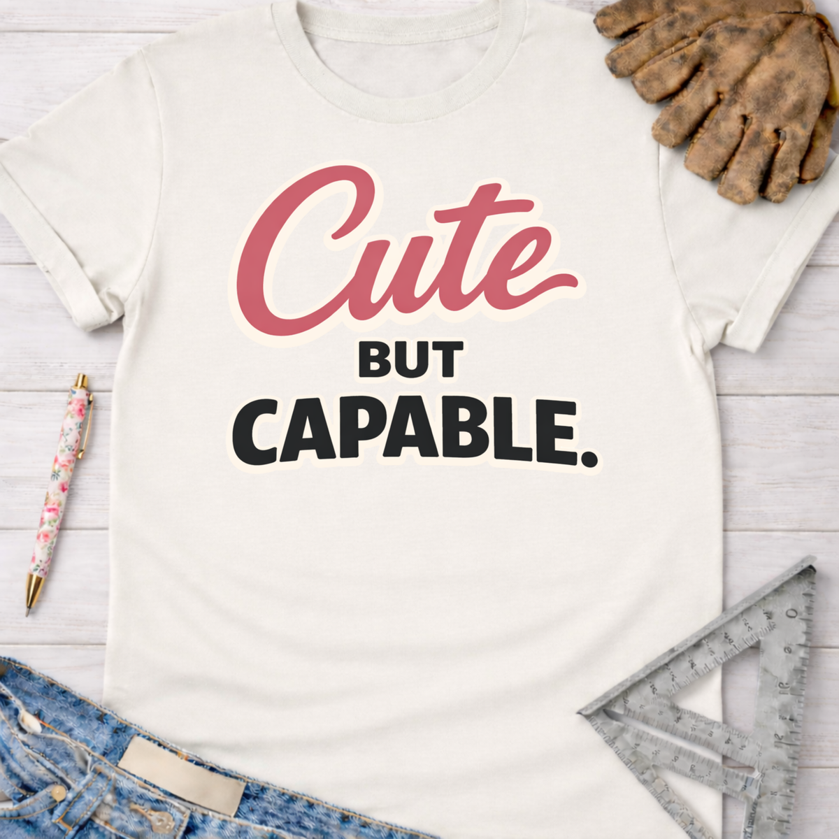 Women's funny woodworking graphic tee shirt for female woodworkers, makers, and DIY builders — Sawdust & Ponytails. Cream cotton tee with "Cute BUT CAPABLE" graphic.