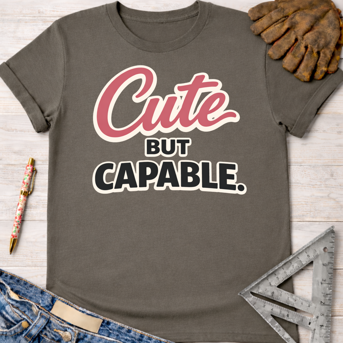Women's funny woodworking graphic tee shirt for female woodworkers, makers, and DIY builders — Sawdust & Ponytails. Dark gray cotton tee with "Cute BUT CAPABLE" in pink and black text.