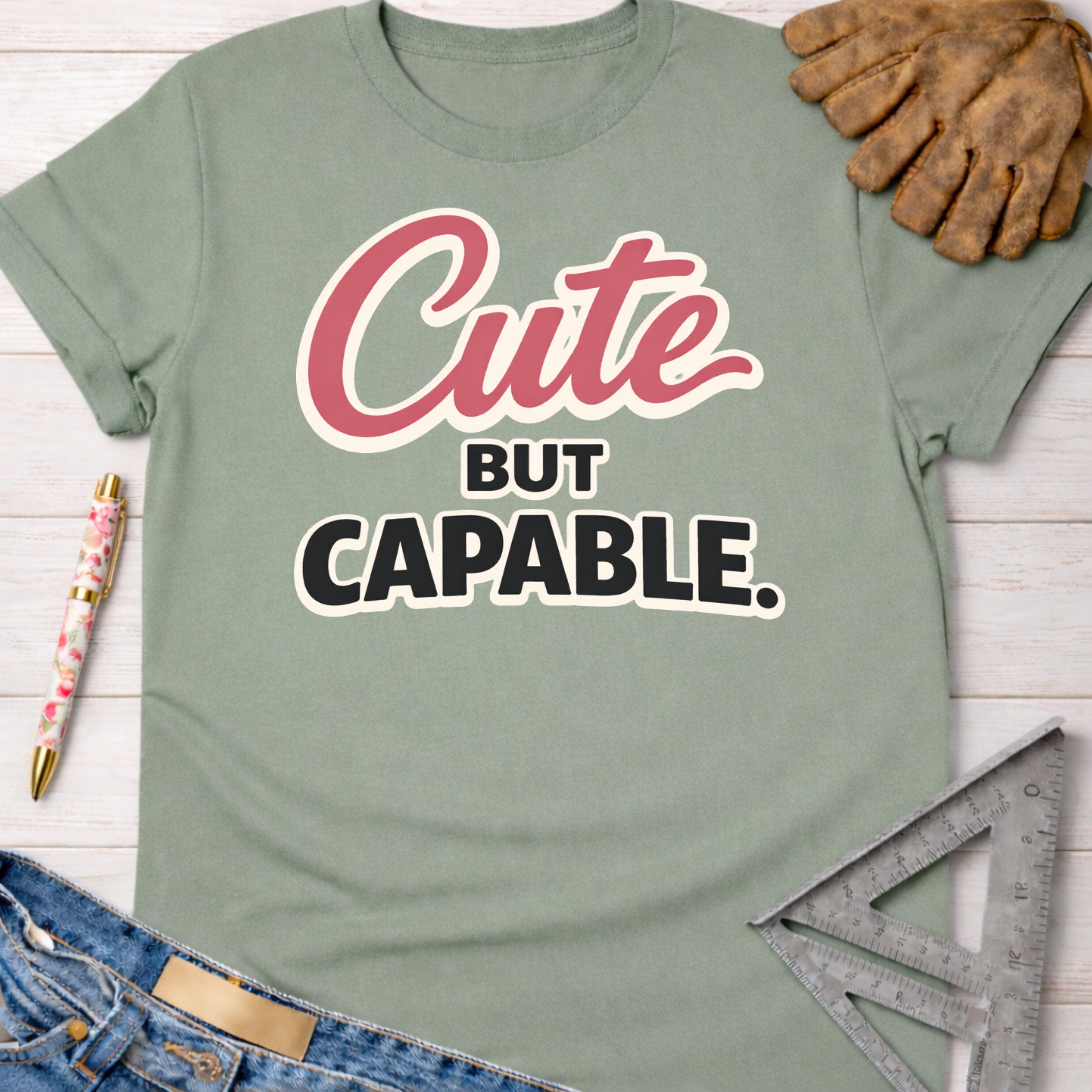 Women's funny woodworking graphic tee shirt for female woodworkers, makers, and DIY builders — Sawdust & Ponytails. Sage green cotton t-shirt with "Cute BUT CAPABLE." graphic.