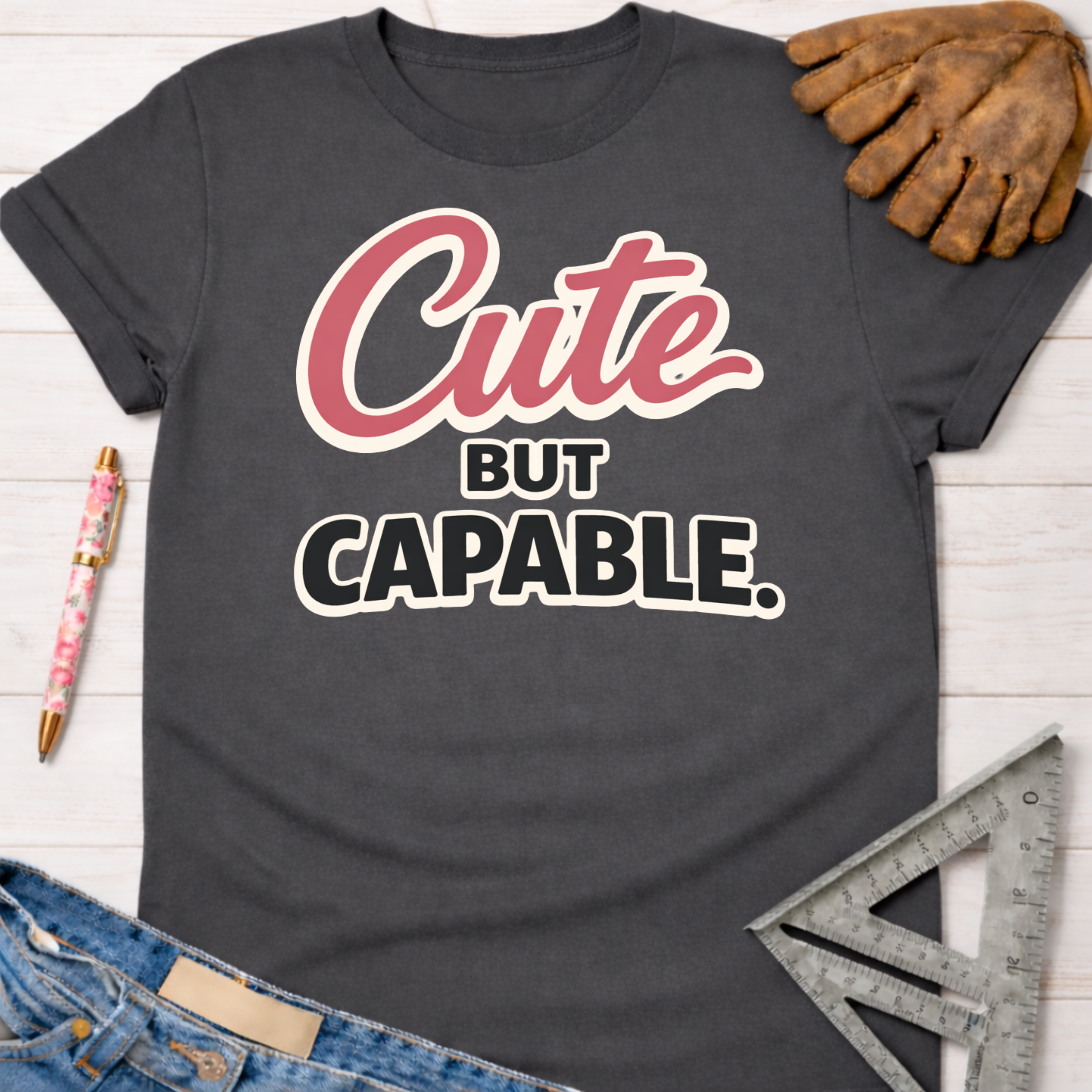 Women's funny woodworking graphic tee shirt for female woodworkers, makers, and DIY builders — Sawdust & Ponytails. Dark gray cotton tee with "Cute BUT CAPABLE" in pink and white text.