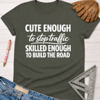 Women's funny woodworking graphic tee shirt for female woodworkers, makers, and DIY builders — Sawdust & Ponytails. Dark gray cotton tee with "Cute Enough To Stop Traffic Skilled Enough To Build The Road" in white text.