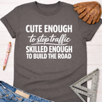 Women's funny woodworking graphic tee shirt for female woodworkers, makers, and DIY builders — Sawdust & Ponytails. Dark gray cotton t-shirt with "Cute Enough To Stop Traffic Skilled Enough To Build The Road" in white text.