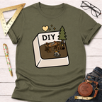 Women's funny woodworking graphic tee shirt for female woodworkers, makers, and DIY builders — Sawdust & Ponytails. Olive green cotton tee with "DIY" computer button graphic featuring a workshop scene.