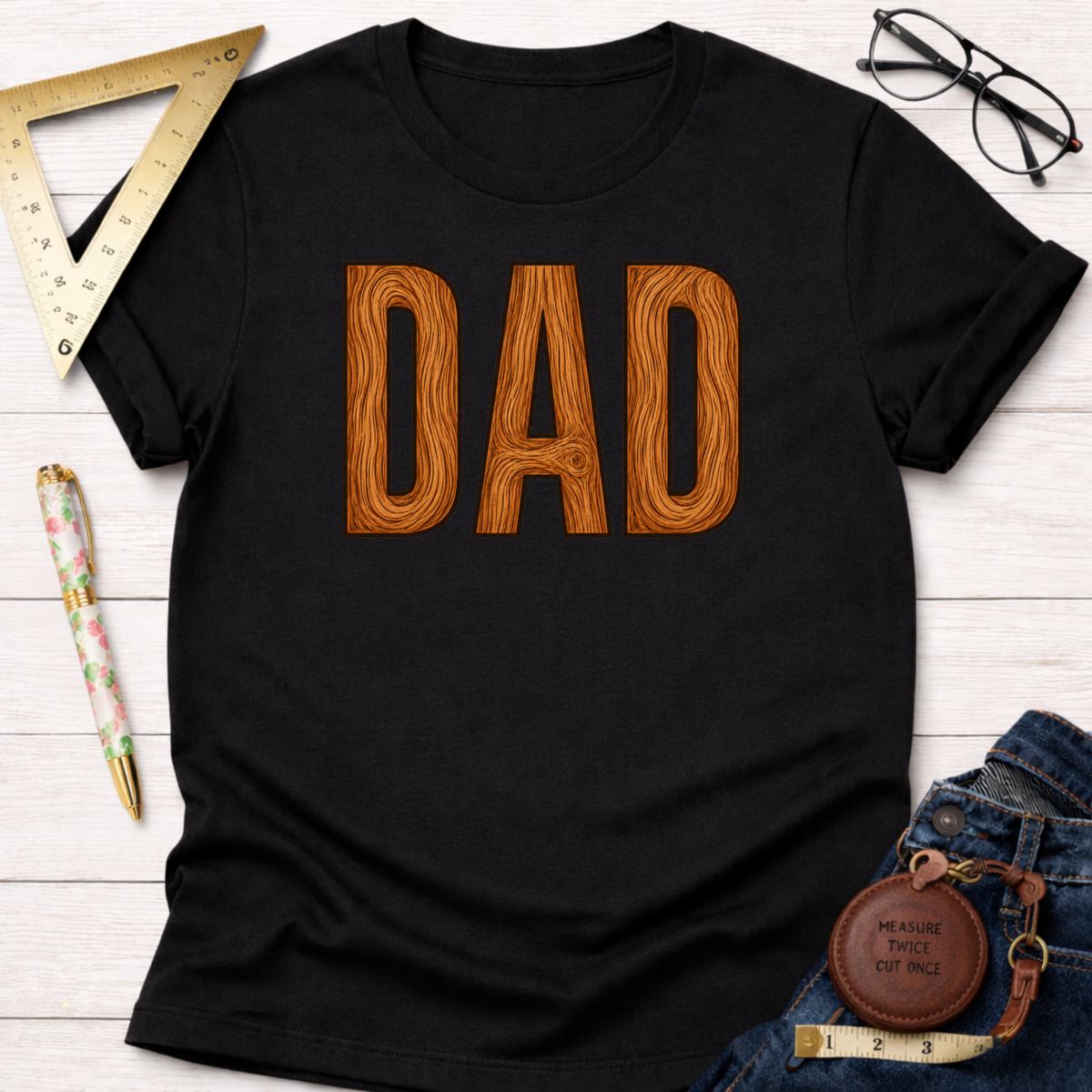 Black cotton t-shirt with "DAD" in a brown wood grain font, styled with jeans and workshop tools.