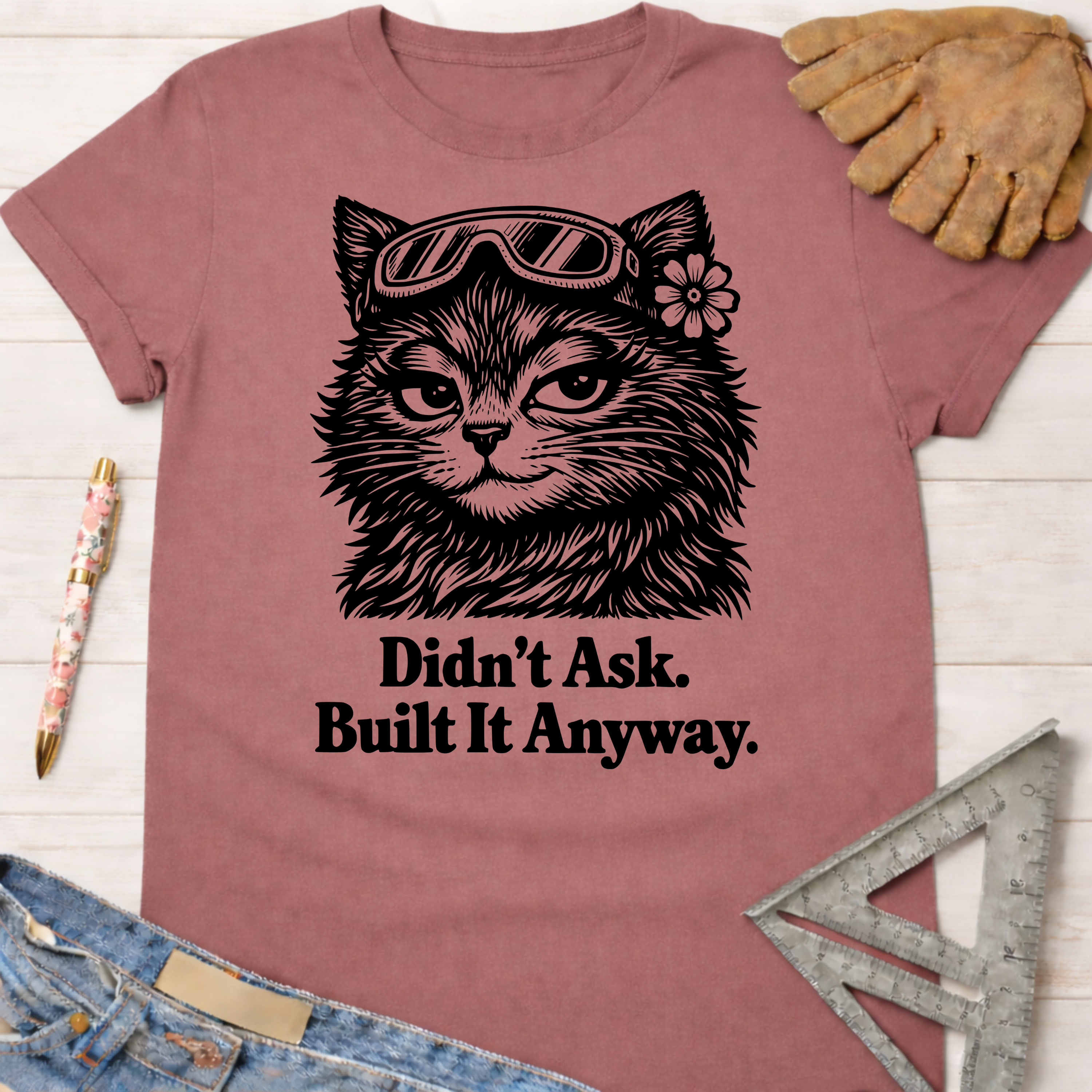 Women's funny woodworking graphic tee shirt for female woodworkers, makers, and DIY builders — Sawdust & Ponytails. Mauve tee with a cat in goggles and "Didn't Ask. Built It Anyway." text.