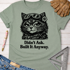 Sage green "Didn't Ask. Built It Anyway." tee with a cat wearing goggles and a flower. Women's funny woodworking graphic tee shirt for female woodworkers, makers, and DIY builders — Sawdust & Ponytails