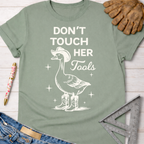 Women's funny woodworking graphic tee shirt for female woodworkers, makers, and DIY builders — Sawdust & Ponytails. Sage green cotton t-shirt with a white graphic of a goose in a cowboy hat and boots, with "Don't Touch Her Tools" text.