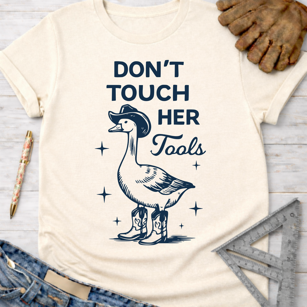Cream t-shirt with a goose in a cowboy hat and boots, "Don't Touch Her Tools" text. Women's funny woodworking graphic tee shirt for female woodworkers, makers, and DIY builders — Sawdust & Ponytails.